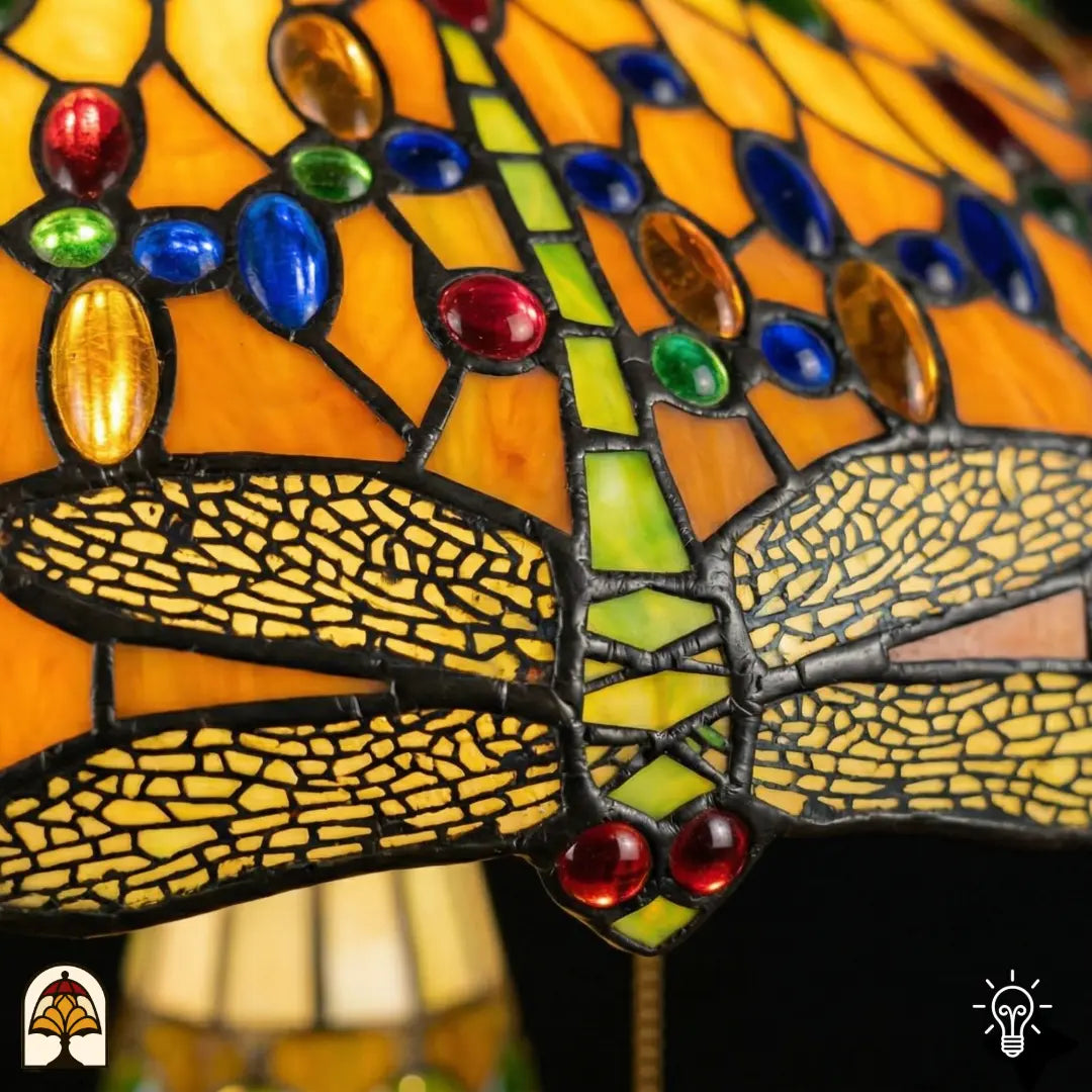 Detailopname van tiffany lamp libelle-rand onderaan de kap verlicht, geel-goudkleurige libellen met geaderde vleugels in glas-in-lood, blauwe en bruine ovale glaskralen en rode ronde kralen