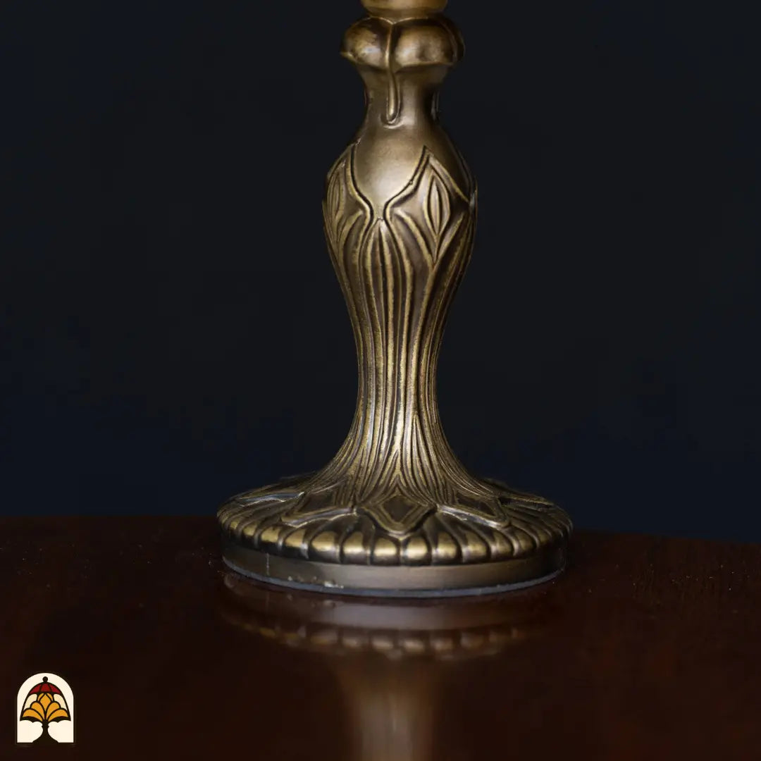 Close-up bronzen Art Nouveau voet tafellamp Libellula Azul ⌀20 op houten tafelblad, donkere achtergrond, fijn bladrelief op steel en voetplaat