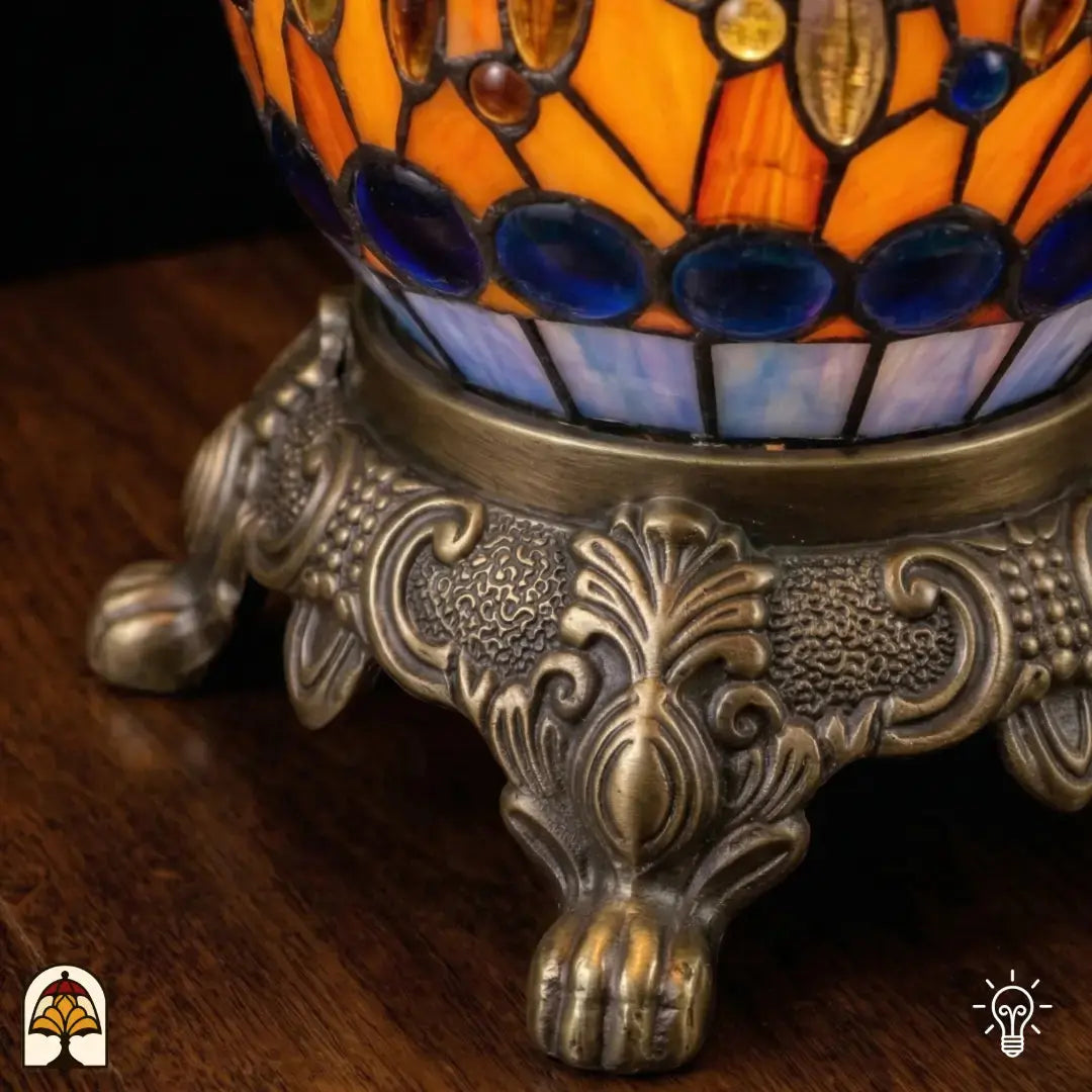Detailopname van tiffany lamp bronzen siervoet met leeuwenpoten en acanthusblad-ornament, oranje en blauw glas-in-lood en blauwe glaskralen bovenaan zichtbaar