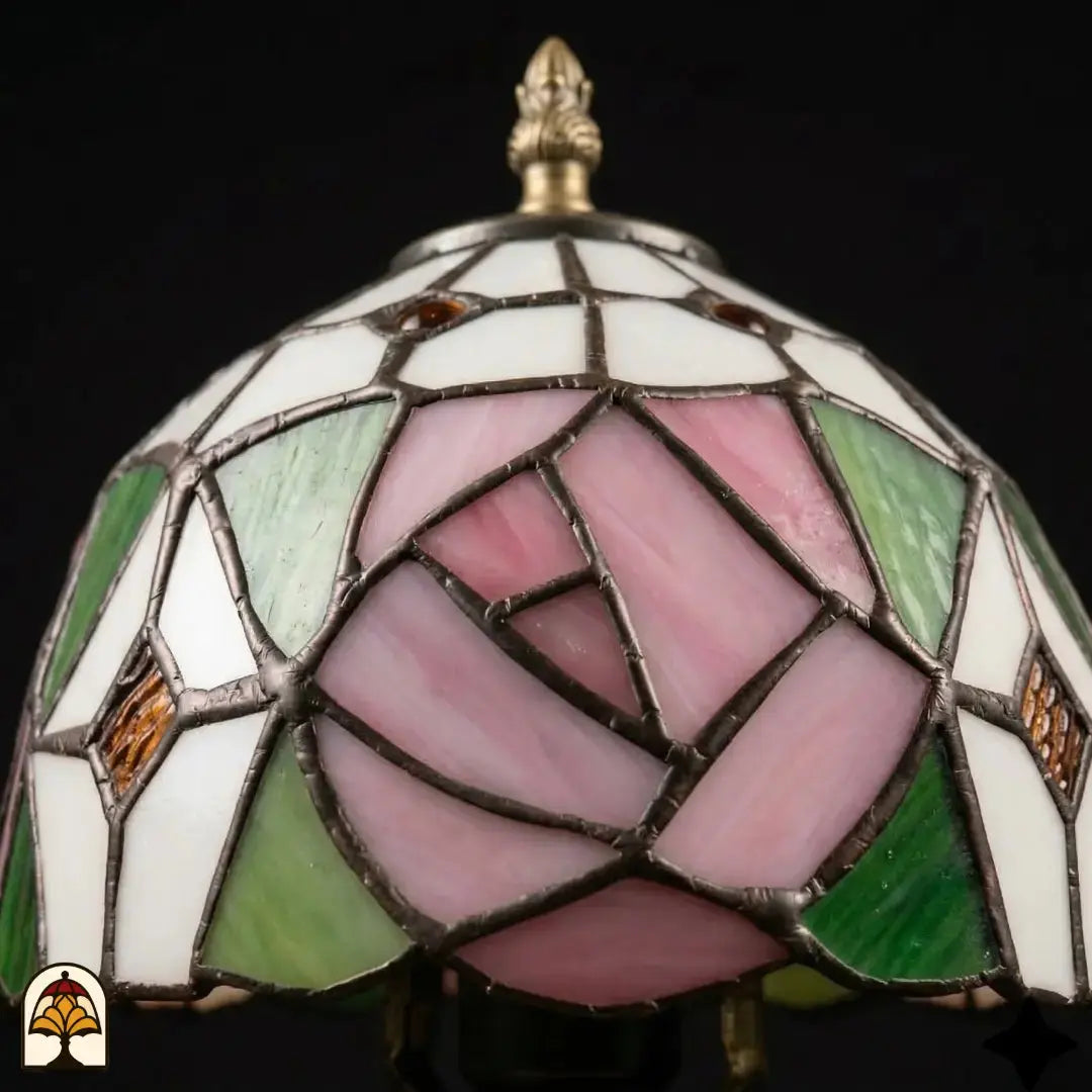 Close-up onverlichte kap Tiffany tafellamp Rosalia Verde, grote roze roos en groene bladeren in glas-in-lood