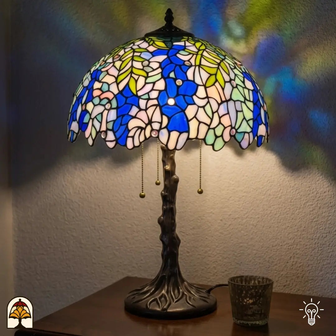 Verlichte Tiffany tafellamp Wisteria Celeste ⌀40 cm in interieur – blauwe en witte glyciniabloemen in glas-in-lood, bronzen boomstam voet, warm licht