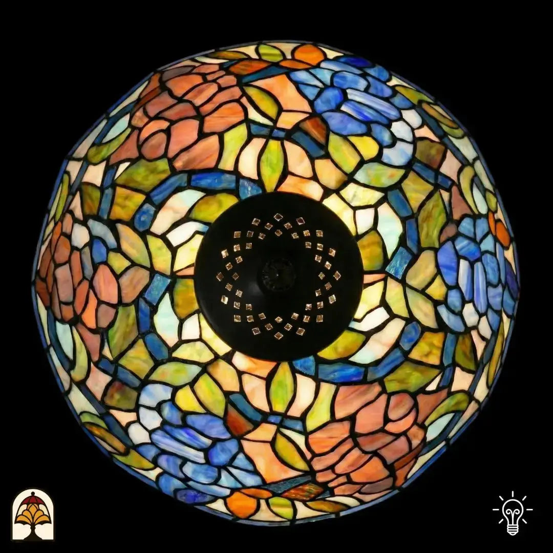 Bovenaanzicht verlichte koepelkap Tiffany tafellamp Florentia Blu, oranje-roze, blauw, groen en beige bladmotieven in glas-in-lood, centrale zwarte fitting zichtbaar