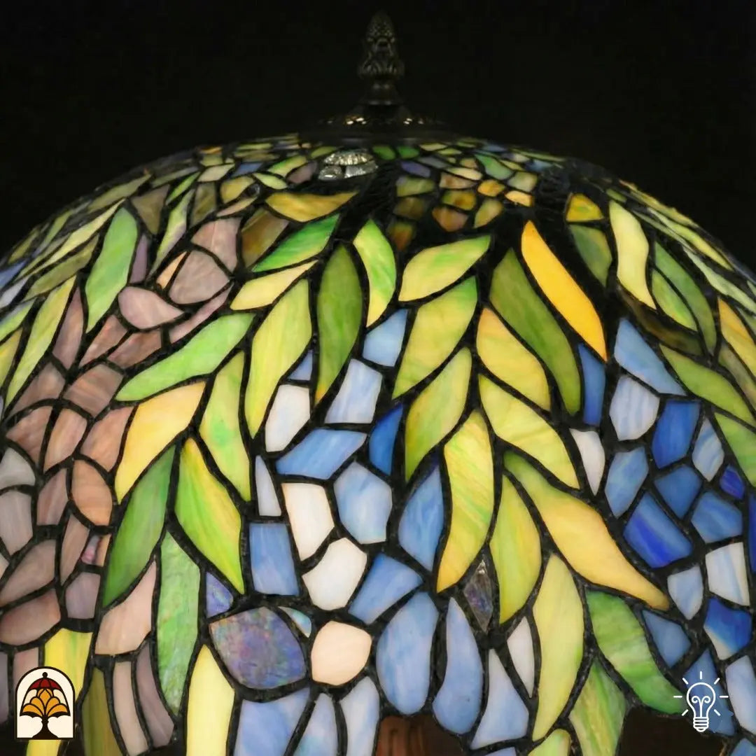 Close-up bovenkant verlichte Tiffany kap — groene bladeren, blauw/paarse en gele glasvlakken