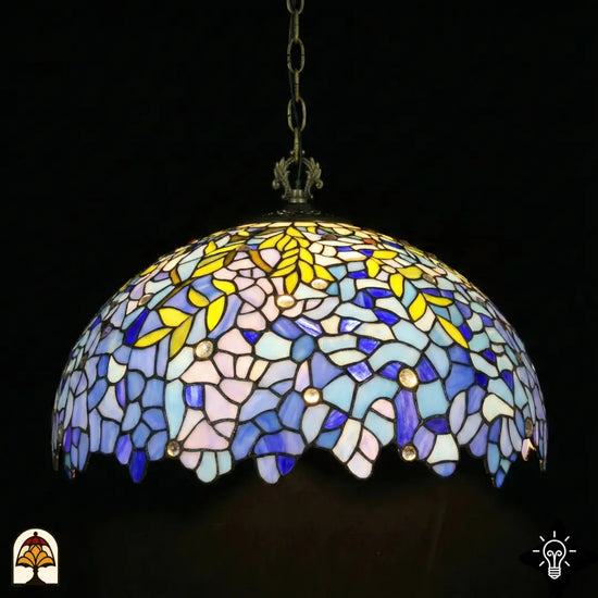 Onverlichte Tiffany hanglamp Drizzle Bleu ⌀50 op donkere achtergrond, koepelkap met lila-blauwe en turquoise glas-in-lood panelen, gele bladmotieven, ronde kristalaccenten, geschulpte onderrand, bronzen ketting