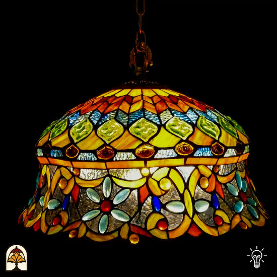 Tiffany lamp hanglamp verlicht van dichterbij, koepelvormige kap met ambergele bovenzone met groene glaskralen en roodbruine ovale kralen, onderzone met gele arabesken, lichtblauwe bloemvormige kralen en rode ronde kralen op transparant glas