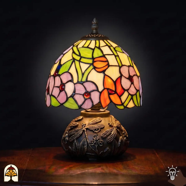 Verlichte Tiffany tafellamp Amber Flora Classic ⌀20 cm op zwarte achtergrond – kap met roze bloesemmotieven op glas-in-lood, bronzen libelle-voet