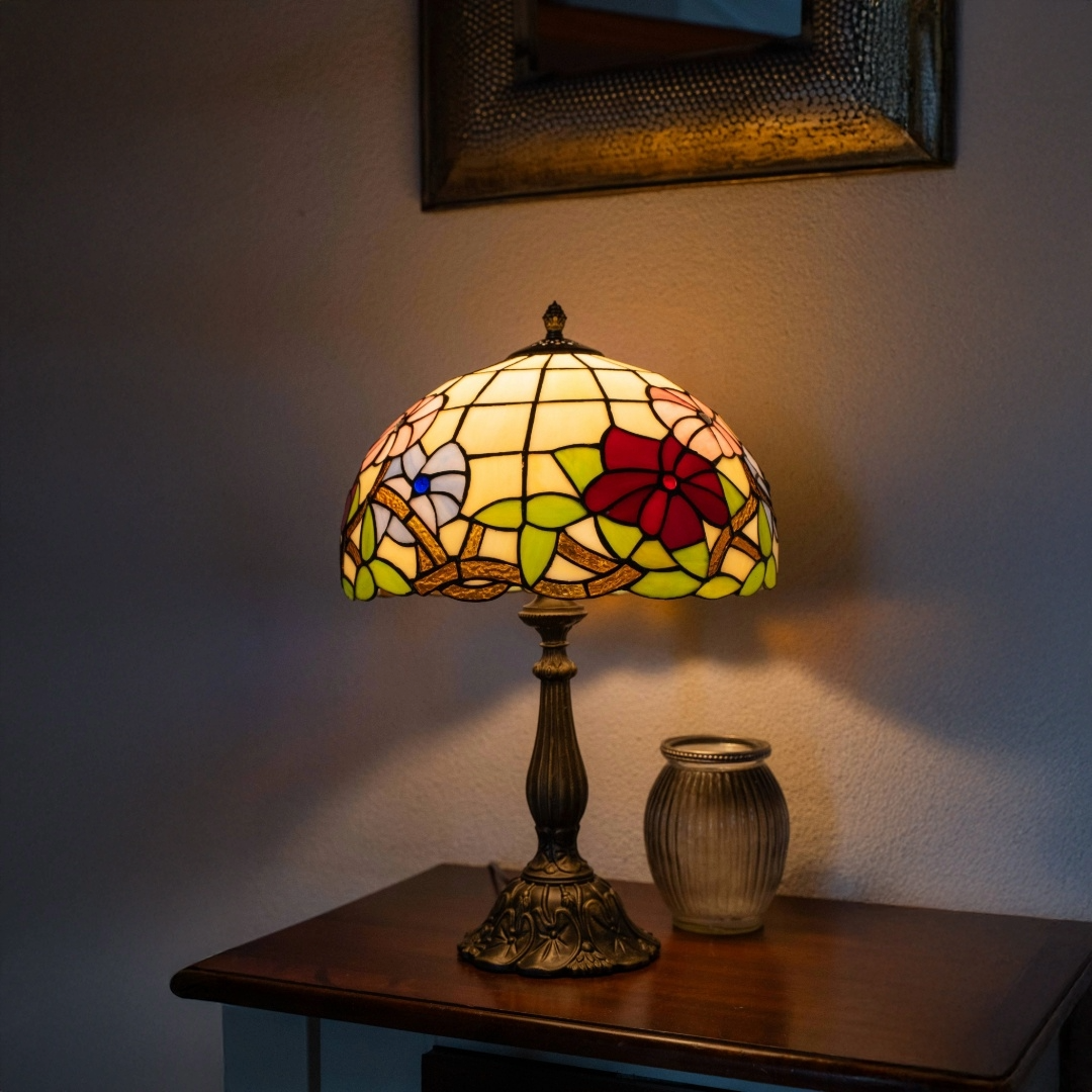 Authentieke Tiffany tafellamp met handgemaakte kap in bloemmotief met rode en roze accenten. Klassieke bronzen voet en warme verlichting, ideaal als sfeerlamp in woonkamer of slaapkamer.