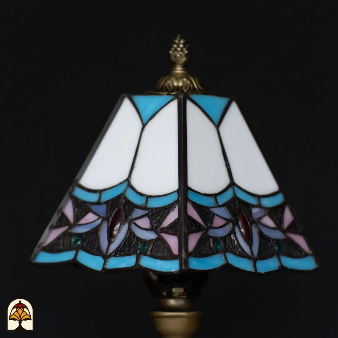 Close-up onverlichte Tiffany kap — witte bovenpanelen, blauwe rand, paarse en roze lotusbloemen, rode edelstenen, getextureerd donker glas