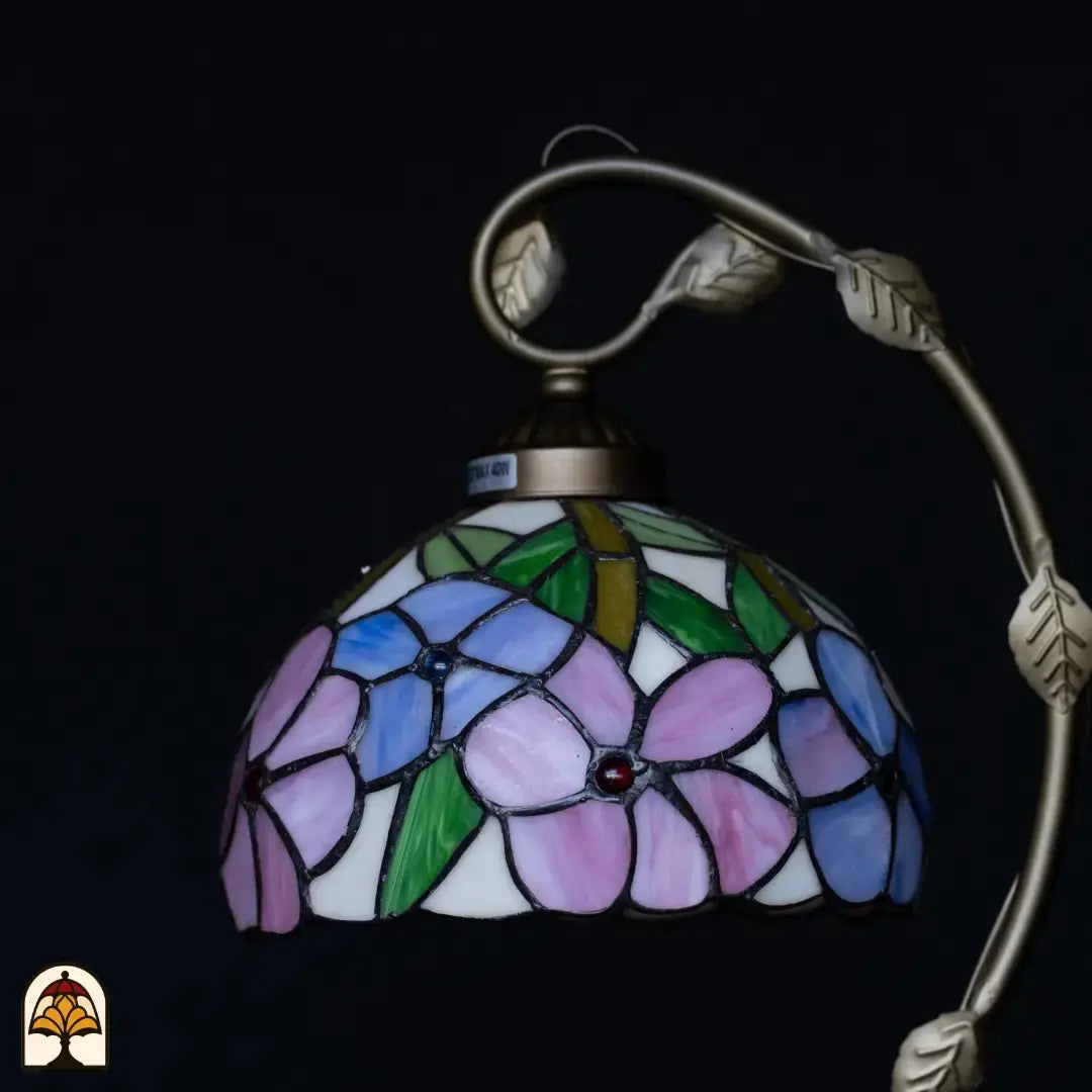 Close-up onverlichte Tiffany kap — blauw/paarse en roze bloemen op witte achtergrond, groene bladeren, rode edelsteentjes