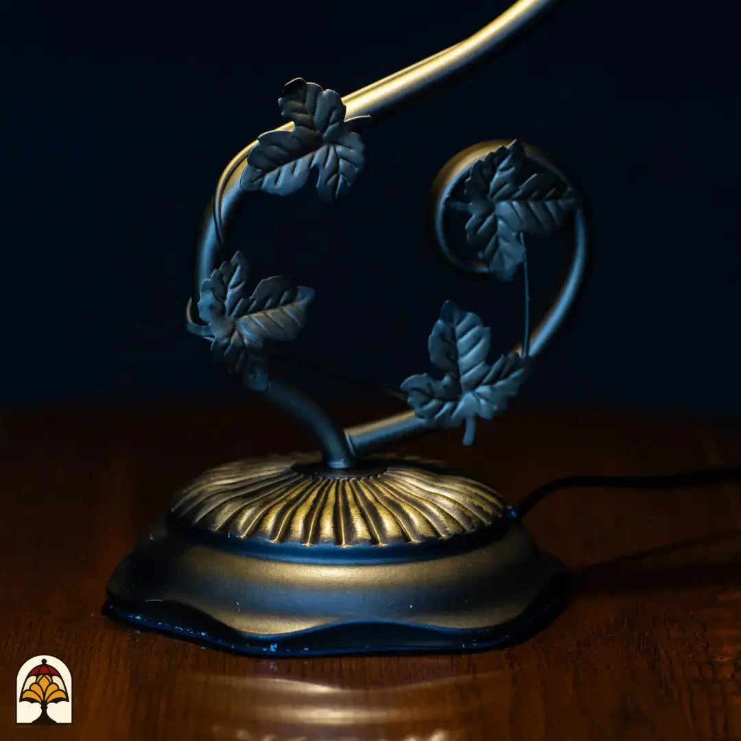 Close-up voet — donkere gebogen arm met bladvormige decoraties, ovale ronde basis met geribbeld goud/brons patroon, aansluitsnoer zichtbaar