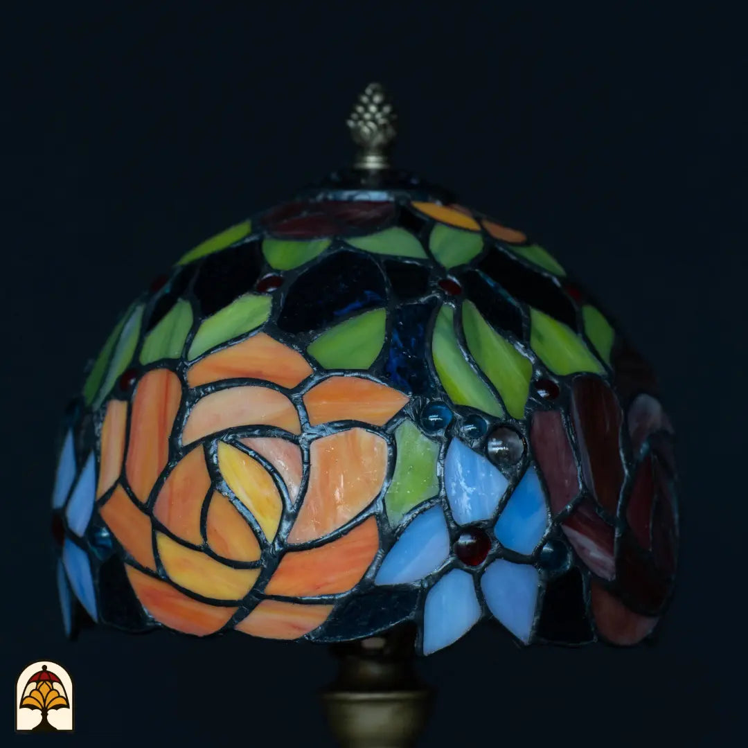 Close-up kap Tiffany tafellamp Fiore onverlicht — oranje en roze rozen, groene bladeren, blauwe en lichtblauwe bloemen, rode edelstenen