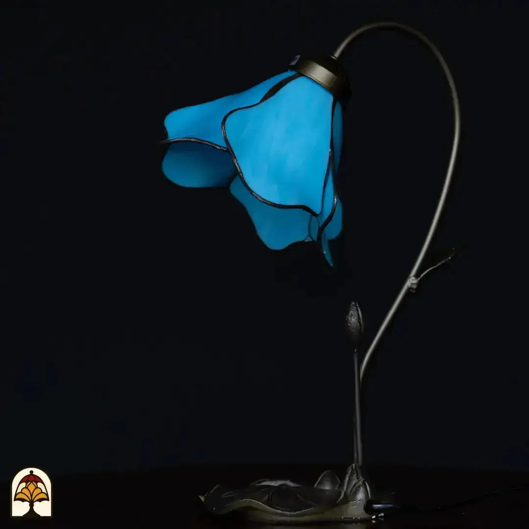 Onverlichte Tiffany tafellamp op donkere achtergrond — blauwe lotusbloem kap, gebogen stengel arm met knop, bronzen lotusblad basis