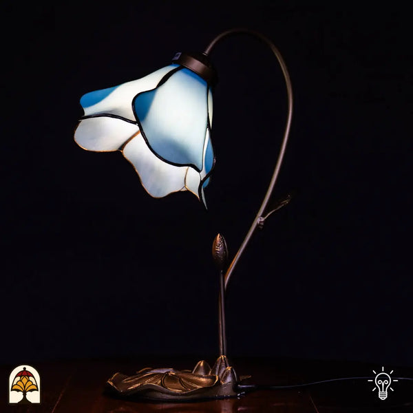 Verlichte Tiffany tafellamp met blauw/witte lotusbloem kap, gebogen stengelvormige arm met knop, bronzen lotusblad basis, zwarte achtergrond