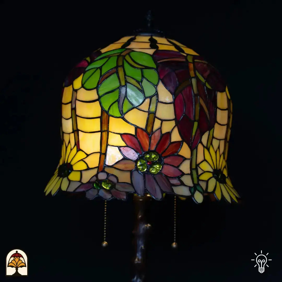 Close-up verlichte Tiffany kap — amber/geel glas met rode en paarse bloemen, groene bladeren en groene edelstenen