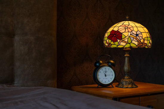 Sfeervolle Tiffany tafellamp met bloemenmotief op een nachtkastje in de slaapkamer, die warm licht uitstraalt naast een klassieke zwarte wekker.