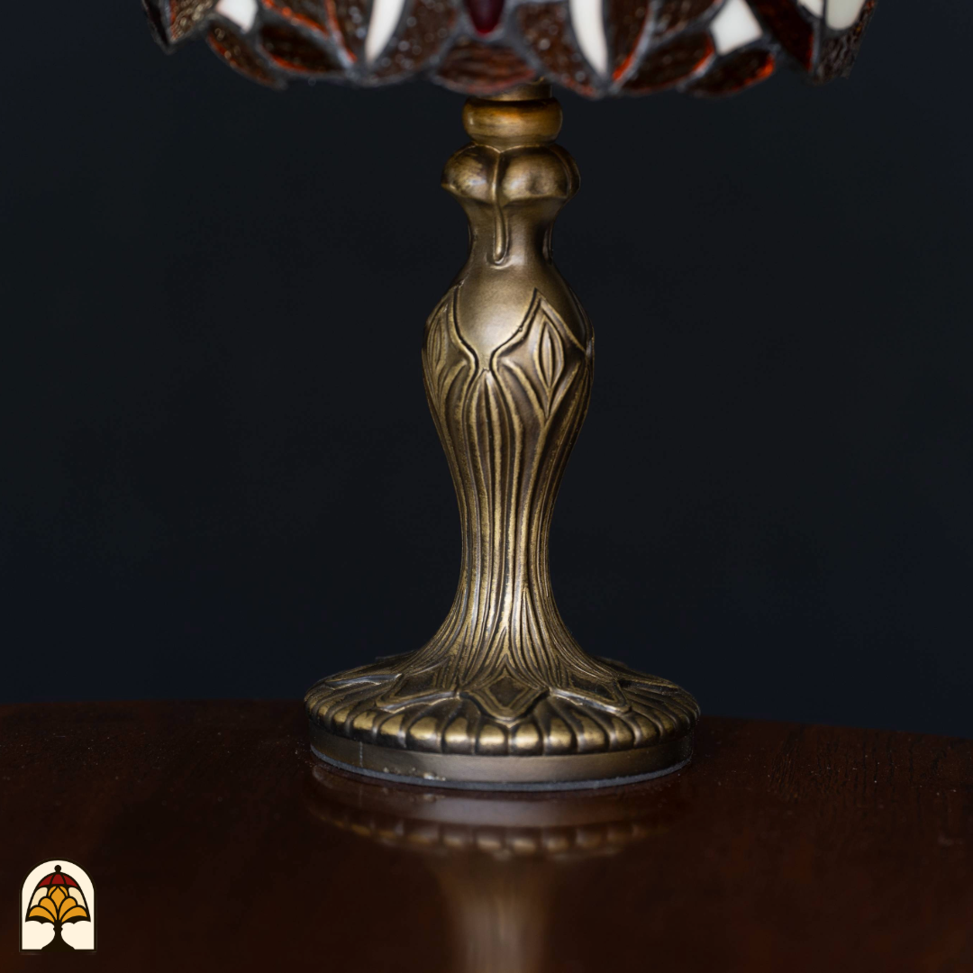 Close-up van de sierlijk vormgegeven antiek bronzen lampvoet van een Tiffany-stijl lamp, geplaatst op een houten oppervlak tegen een zwarte achtergrond.