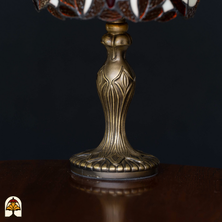 Close-up van de sierlijk vormgegeven antiek bronzen lampvoet van een Tiffany-stijl lamp, geplaatst op een houten oppervlak tegen een zwarte achtergrond.