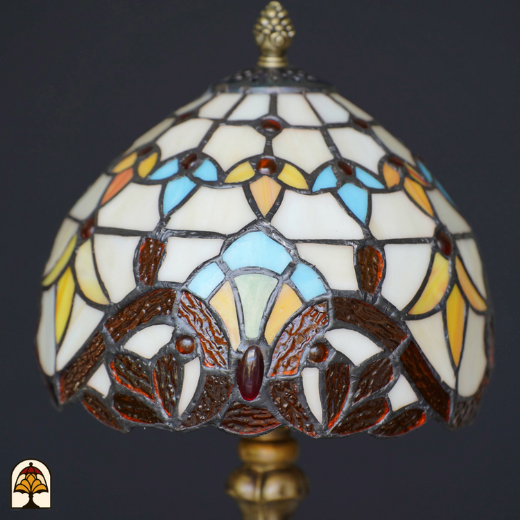 Nabijbeeld van een Tiffany-stijl lampenkap met glas-in-lood in zachte pastelkleuren, warme geel- en bruintinten en gedetailleerde koperlijnen.