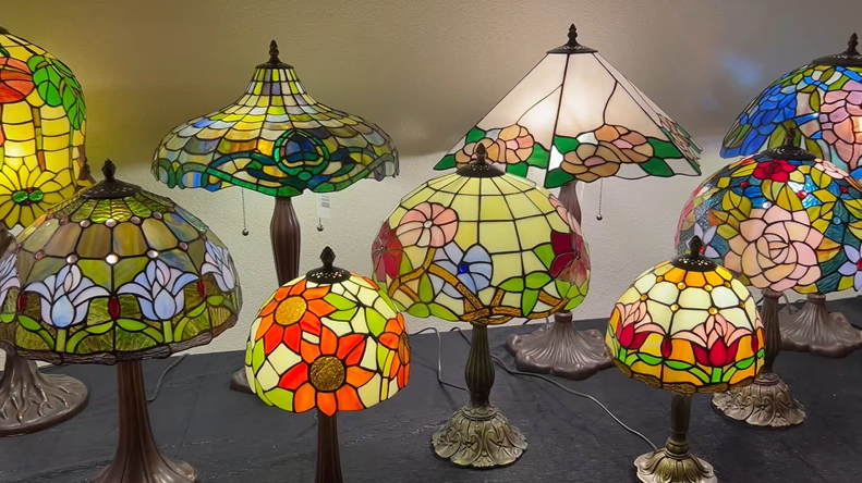 Video laden: Een collectie authentieke handgemaakte Tiffany lampen van De Sierkamer, waaronder diverse Tiffany tafellampen met kleurrijke bloemmotieven in glas-in-lood.