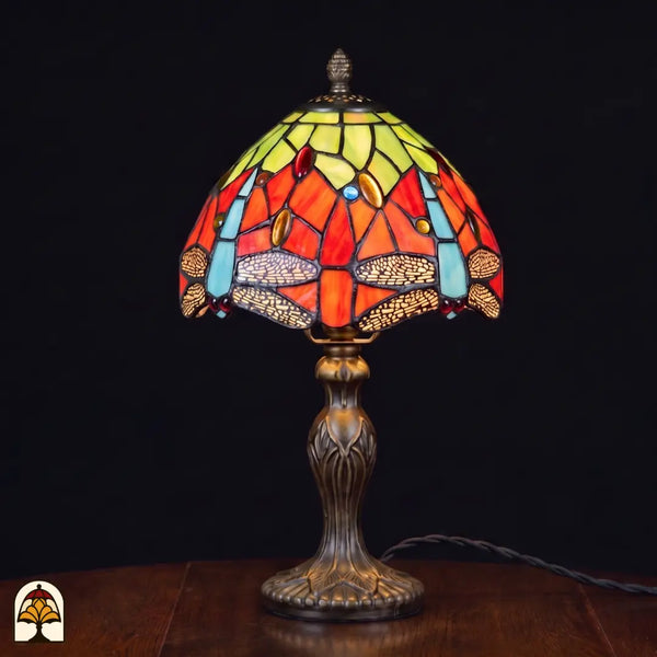 Verlichte Tiffany lamp tafellamp Libellula Azul ⌀20 cm op donkere achtergrond – oranje kap met groene bovenpanelen, blauwe libellenfries, gekleurde juwelen, bronzen Art Nouveau voet