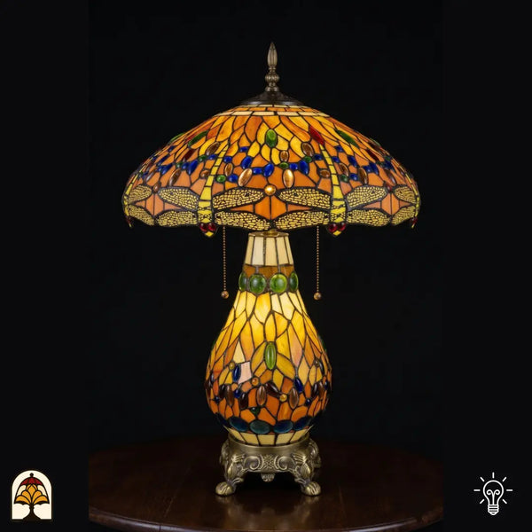 Tiffany lamp tafellamp verlicht, koepelvormige amberkleurige glas-in-lood kap met libellemotieven langs de rand, blauwe en groene ovale glaskralen, trekkettingschakelaar; peervormige glas-in-lood voet en bronzen siervoet met leeuwenpoten