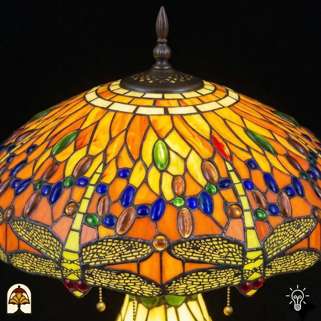 Detailopname van tiffany lamp kapbovenzone verlicht, amberkleurig glas met blauwe en groene ovale glaskralen in een band en rode ronde kralen, bronzen ventilatieplaat en puntfinial bovenaan