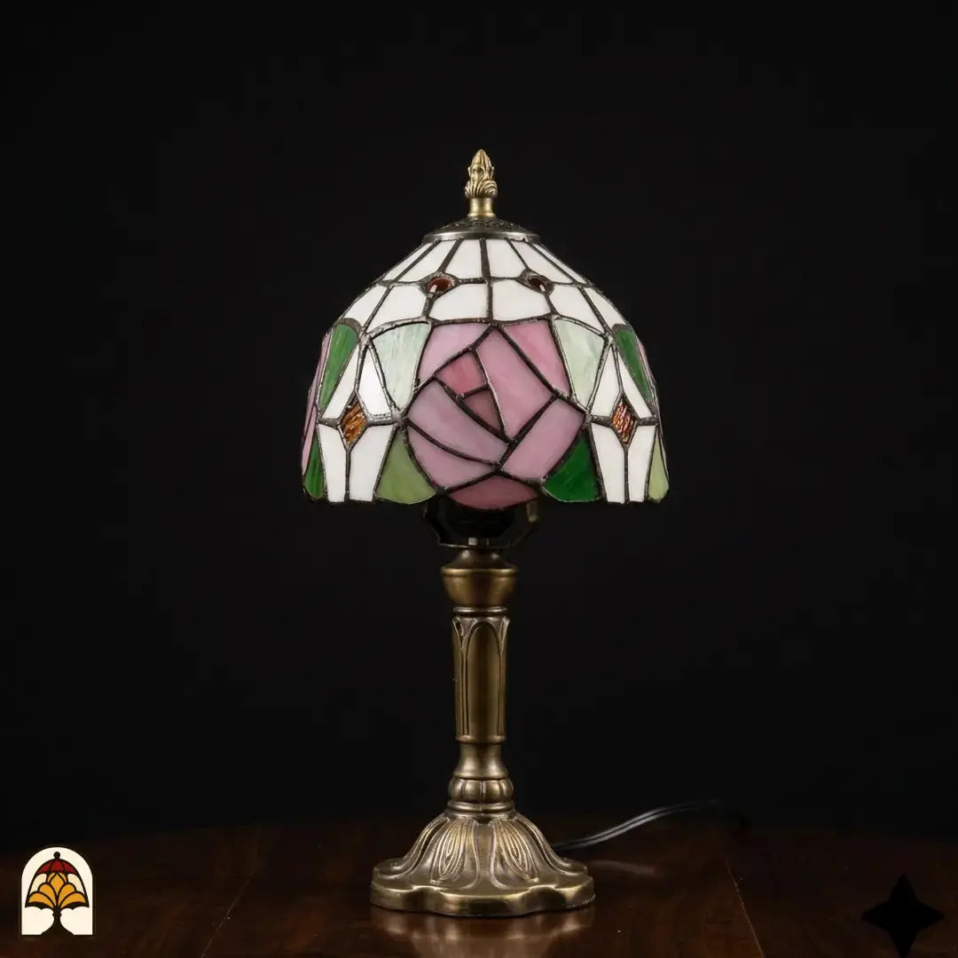 Onverlichte Tiffany tafellamp Rosalia Verde, witte kap met roze roos en groene bladeren in glas-in-lood, bronzen slanke vaasvoet, donkere achtergrond