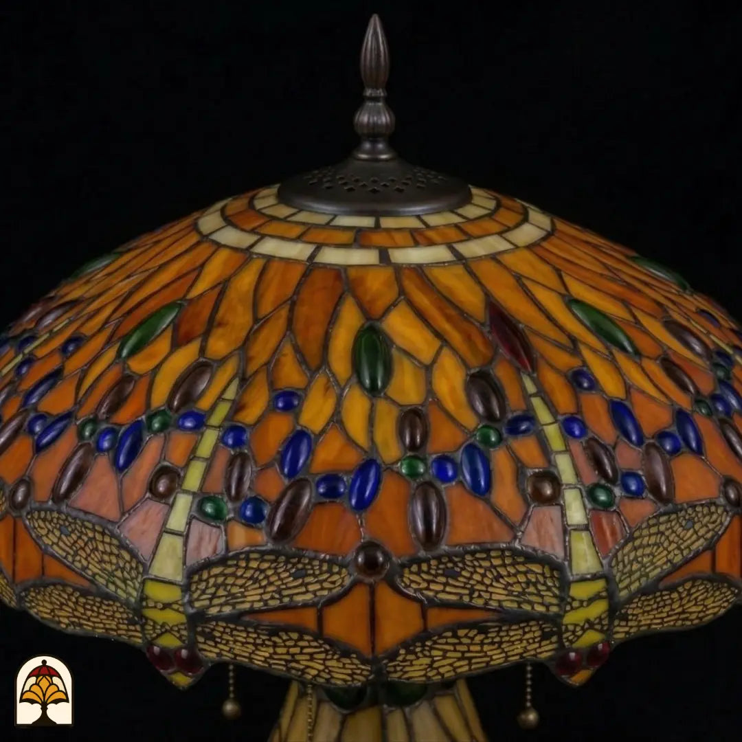 Detailopname van tiffany lamp kapbovenzone onverlicht, amberkleurig glas met blauwe, groene en bruine ovale glaskralen in banden, trekkettingen en bronzen ventilatieplaat zichtbaar