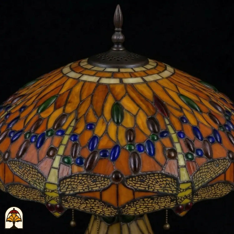 Detailopname van tiffany lamp kapbovenzone onverlicht, amberkleurig glas met blauwe, groene en bruine ovale glaskralen in banden, trekkettingen en bronzen ventilatieplaat zichtbaar