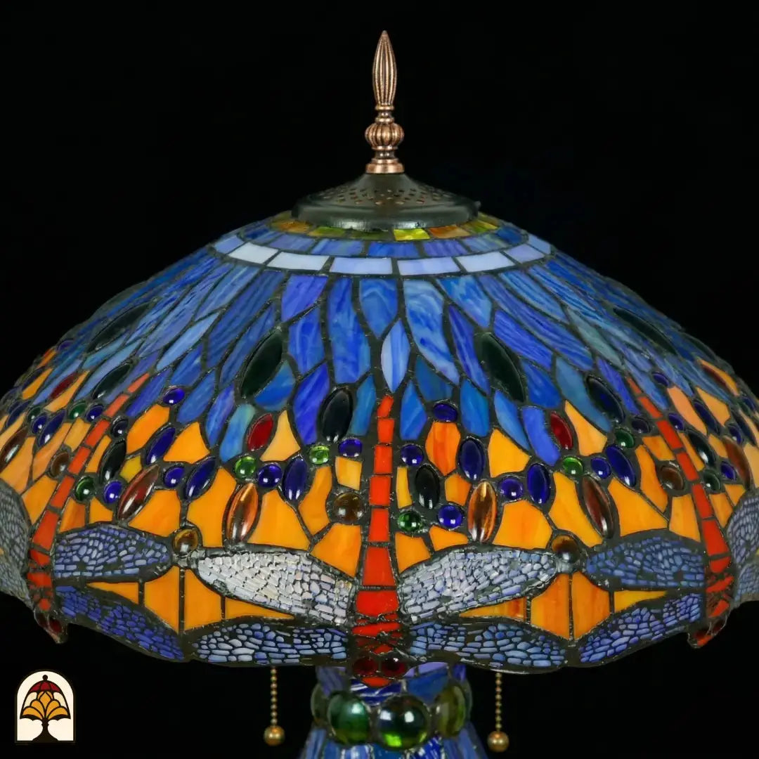 Detailopname van tiffany lamp kapbovenzone onverlicht, blauw en lichtblauw glas met blauwe, groene en amber ovale glaskralen in banden, puntfinial en bronzen ventilatieplaat bovenaan zichtbaar
