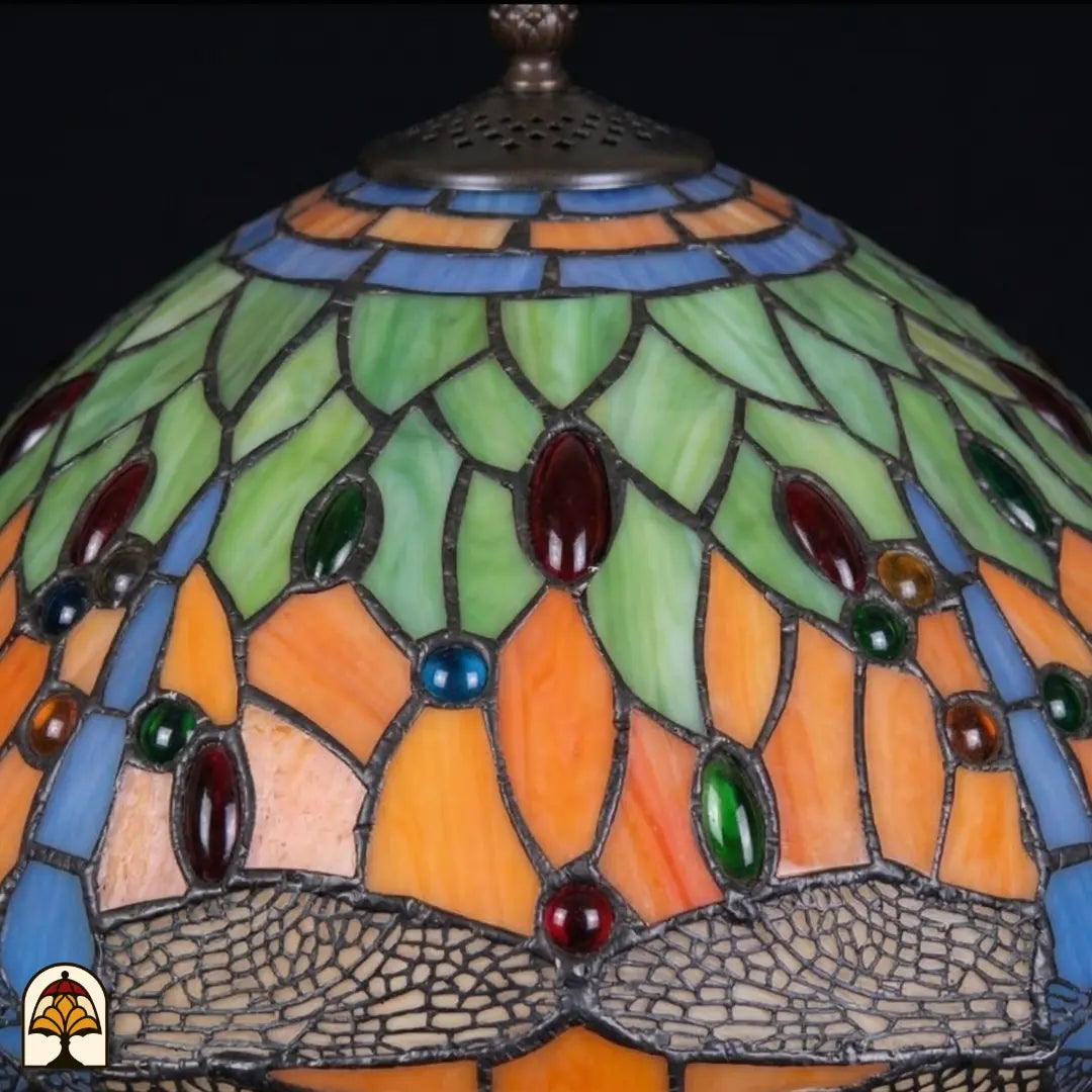 Close-up onverlichte kap Libellula Azul ⌀30, oranje panelen met groene bladmotieven, blauwe glasstroken, rode en groene juwelen en libellenfries langs de rand