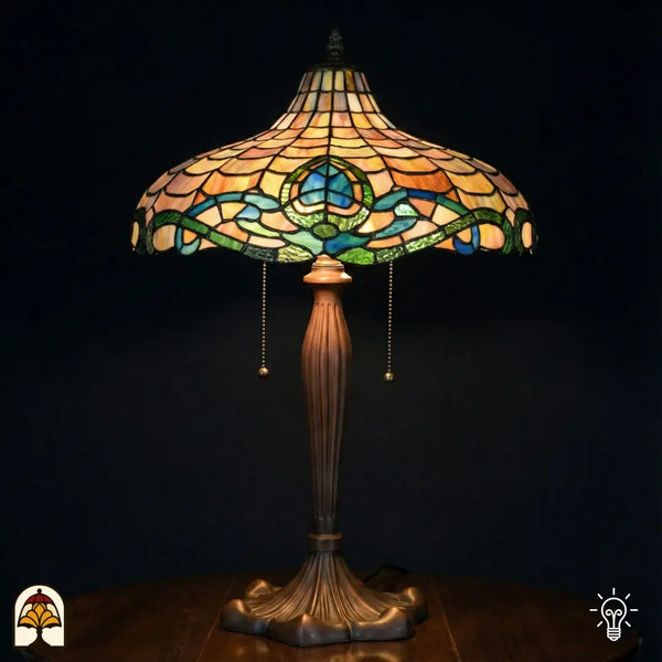 Verlichte grote Tiffany tafellamp met brede schaalvormige kap met amber schubpatroon, turquoise/blauwe en groene Art Nouveau-rand met lotusmotief, bronzen geribbelde voet met trekschakelaars, donkere achtergrond