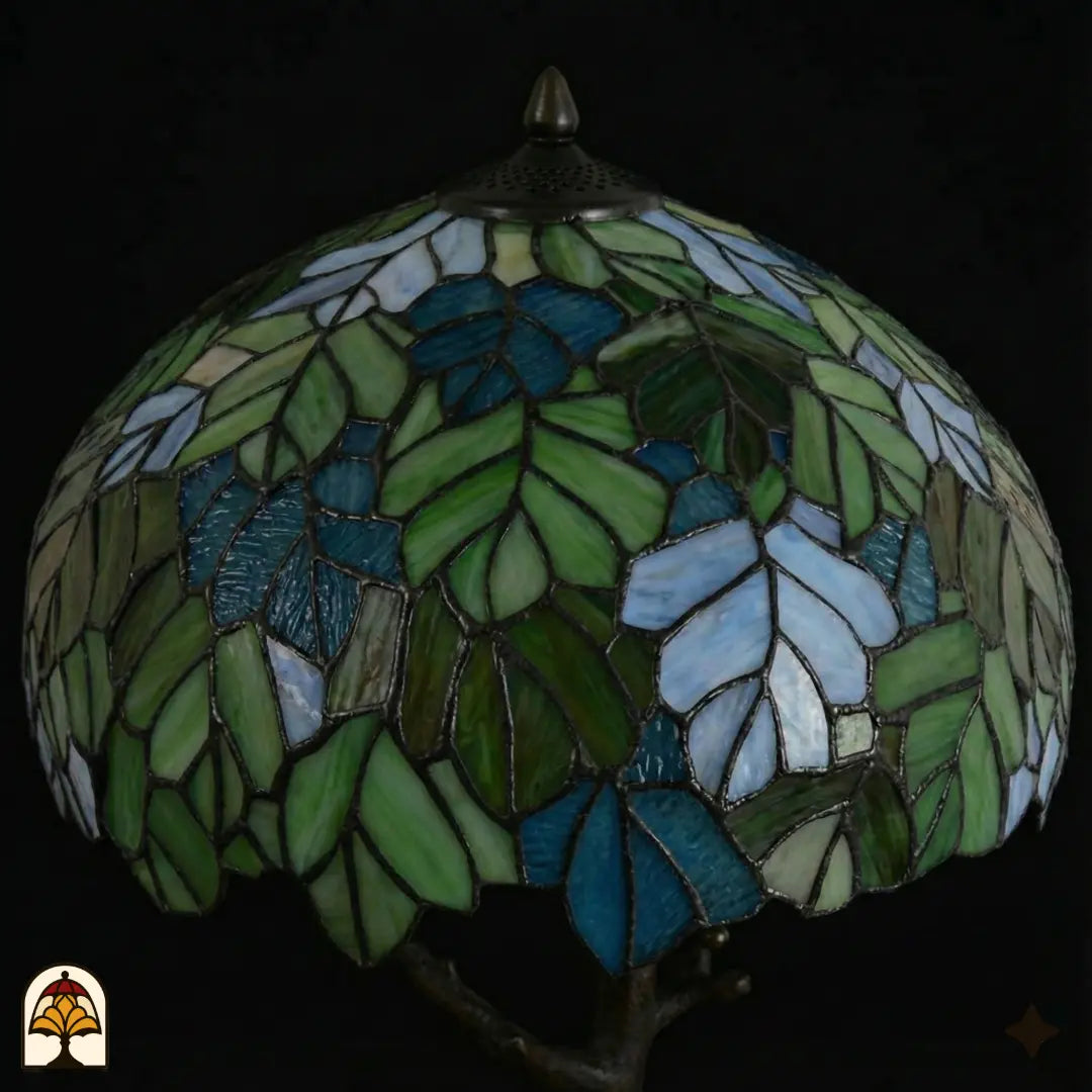 Close-up onverlichte koepelkap Tiffany tafellamp Sylva Verde, groen-blauwe en wit-lichtblauwe bladmotieven in glas-in-lood