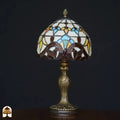 Onverlichte Tiffany tafellamp Baroque op zwarte achtergrond – koepelkap met crème, lichtblauw, geel en bruine barokke bladvormen, rode edelsteen
