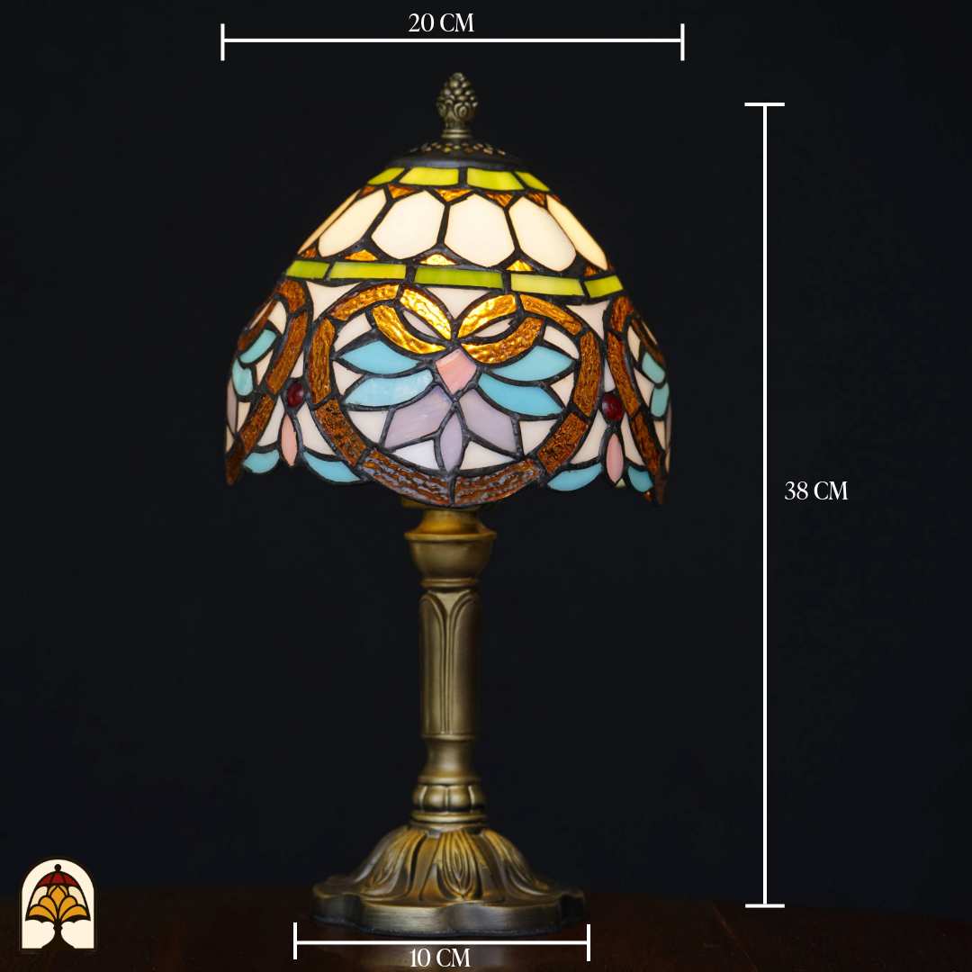 Brandende Tiffany-stijl tafellamp met glas-in-lood kap in wit, geel, groen, pastelblauw en roze, op een bronzen voet. Afmetingen: hoogte 38 cm, kapdiameter 20 cm, voetdiameter 10 cm, tegen een zwarte achtergrond.