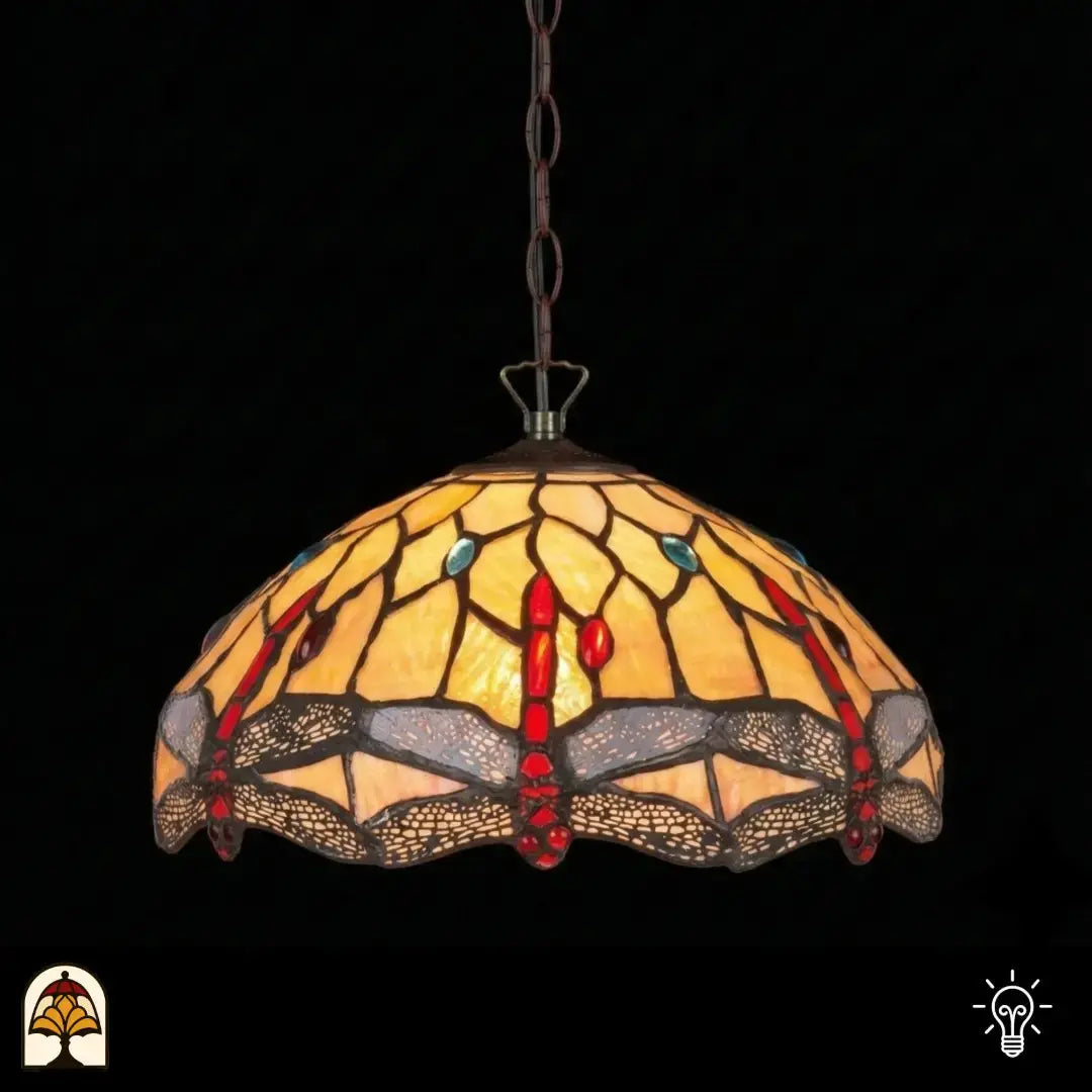 Verlichte Tiffany hanglamp Libelle, koepelvormige geel-amber kap met rode druppelvormige accenten, blauwe details en libellenmotieven in glas-in-lood, donkere achtergrond