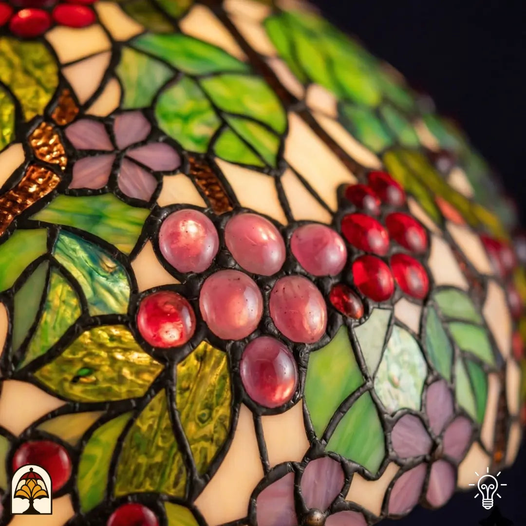 Close-up verlichte kap Tiffany hanglamp Sylva Berria, roze en rode druivenkorrels in glas-in-lood met gedetailleerde knobbels, groene bladeren en bruine wijnranken