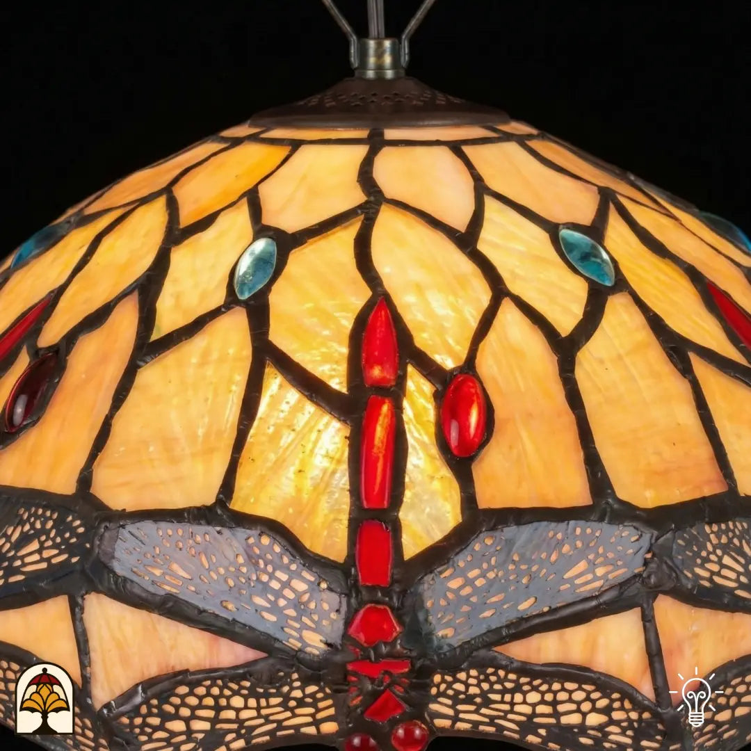 Close-up verlichte kap Tiffany hanglamp Libelle, geel-amber glas-in-lood met rode druppels en blauwe accenten, libellenmotieven langs de rand