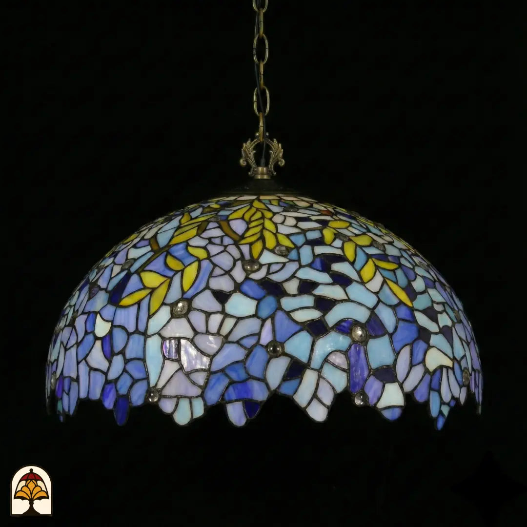 Onverlichte Tiffany hanglamp Drizzle Bleu ⌀50 op donkere achtergrond, lila-blauwe en turquoise koepelkap met gele bladaccenten en geschulpte rand, bronzen ketting