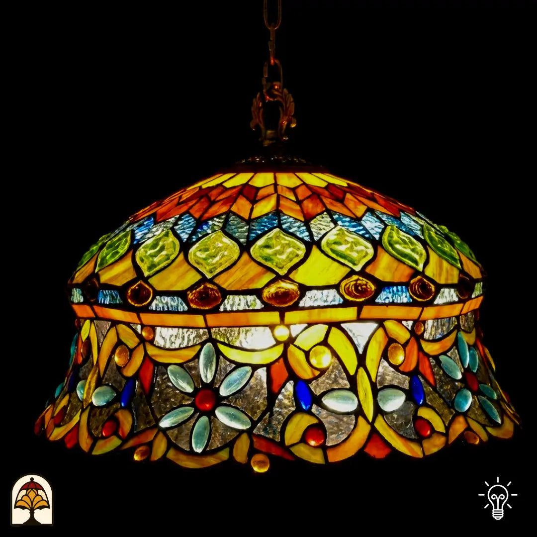 Tiffany lamp hanglamp verlicht van dichterbij, koepelvormige kap met ambergele bovenzone met groene glaskralen en roodbruine ovale kralen, onderzone met gele arabesken, lichtblauwe bloemvormige kralen en rode ronde kralen op transparant glas