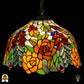 Tiffany lamp hanglamp verlicht van dichterbij, koepelvormige kap met oranje rozen, rode ovale glaskralen, gele rozen en groene bladeren op witte getextureerde achtergrond, opgehangen aan bronzen ketting