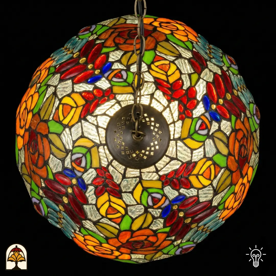 Bovenaanzicht van tiffany lamp hanglamp verlicht, ronde koepel met symmetrisch patroon van oranje en gele rozen, rode glaskralen en groene bladeren, centrale bronzen ventilatieplaat zichtbaar
