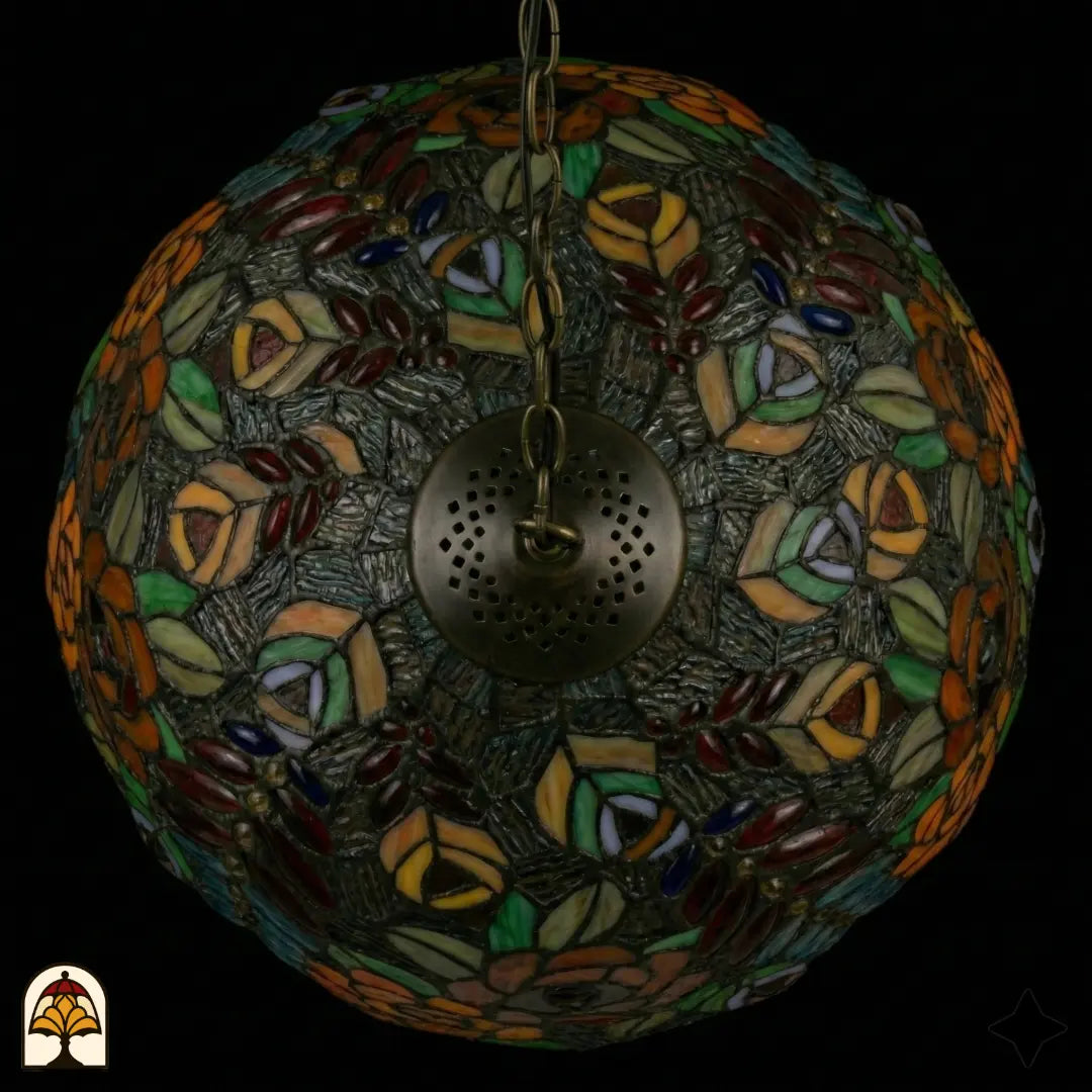 Bovenaanzicht van tiffany lamp hanglamp onverlicht, koepel met symmetrisch patroon van oranje en roze rozen, gekleurde bladeren en glaskralen op getextureerd grijs glas, bronzen ventilatieplaat zichtbaar