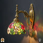 Verlichte Tiffany wandlamp Floral Garden op gebogen bronzen arm, kap met rode en roze bloemen, groene bladeren en gele accenten in glas-in-lood
