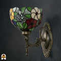 Onverlichte Tiffany wandlamp Floral Garden van opzij, kap met groene bladeren, rode, witte en gele bloemen en grijze druppels in glas-in-lood