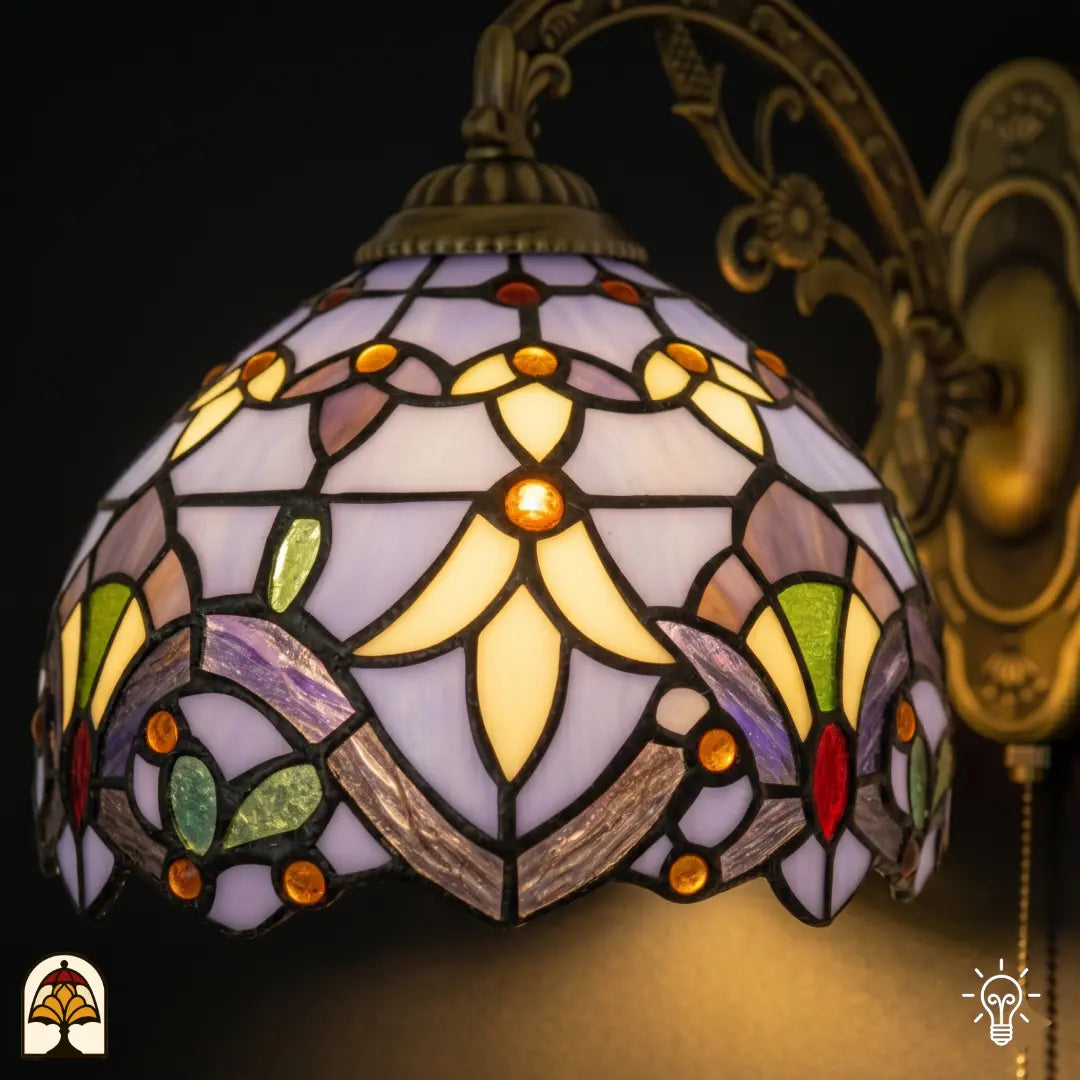 Close-up verlichte kap Tiffany wandlamp Royal Mosaic – lavendelblauwe en crèmegele glas-in-lood vlakken met oranje, rode en paarse juwelen