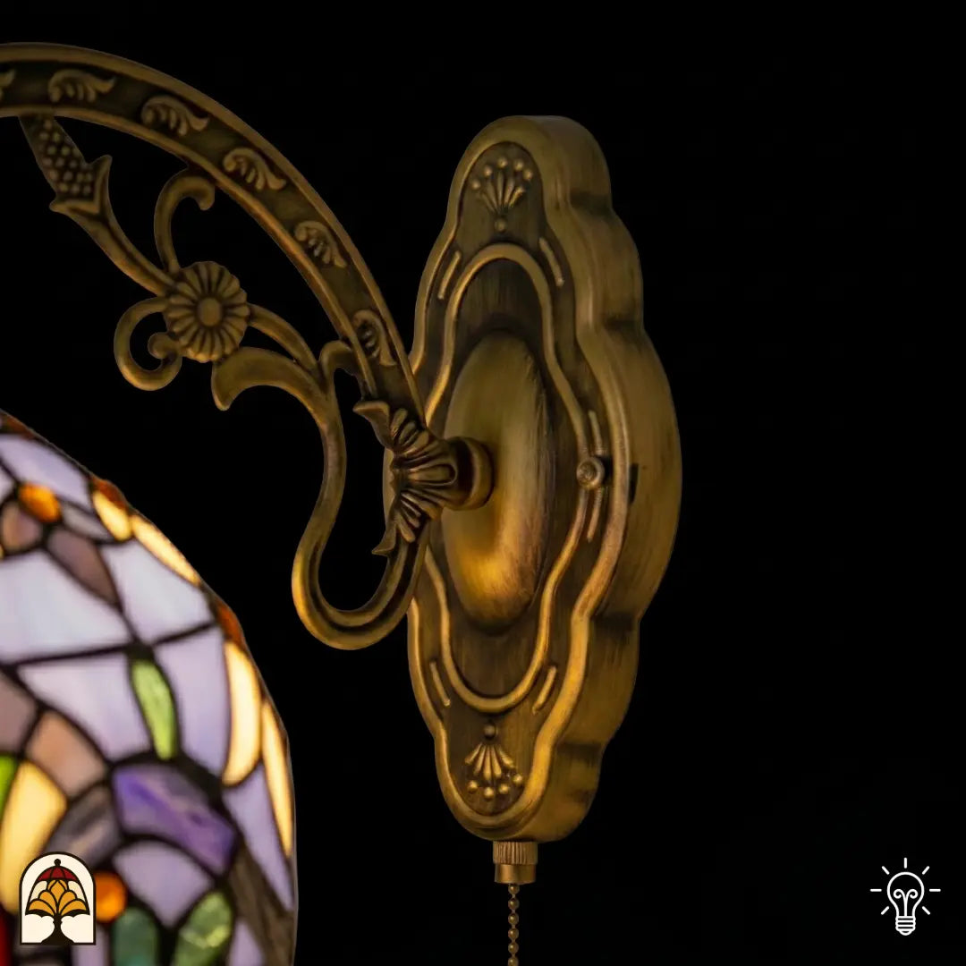 Close-up bronzen wandbeugel Tiffany wandlamp Royal Mosaic met sierlijk gevormde wandplaat en gegoten reliëf, gebogen arm met druif- en bloemversiering