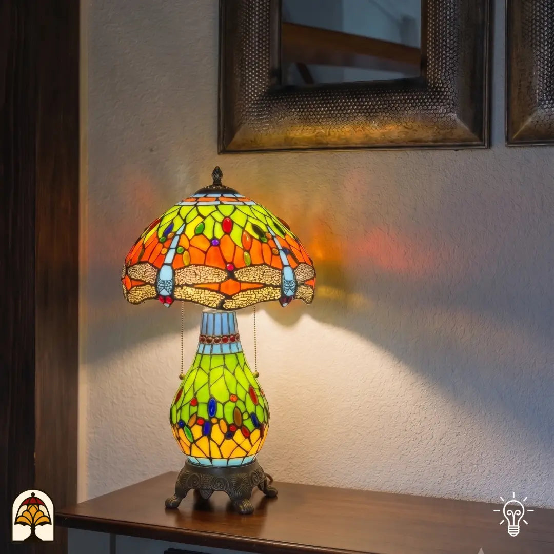 Verlichte Tiffany tafellamp Libellula Lumina ⌀30 cm in interieur – oranje en geel-groene glas-in-lood kap met libellenmotief, bronzen leeuwenpootvoet, warm licht
