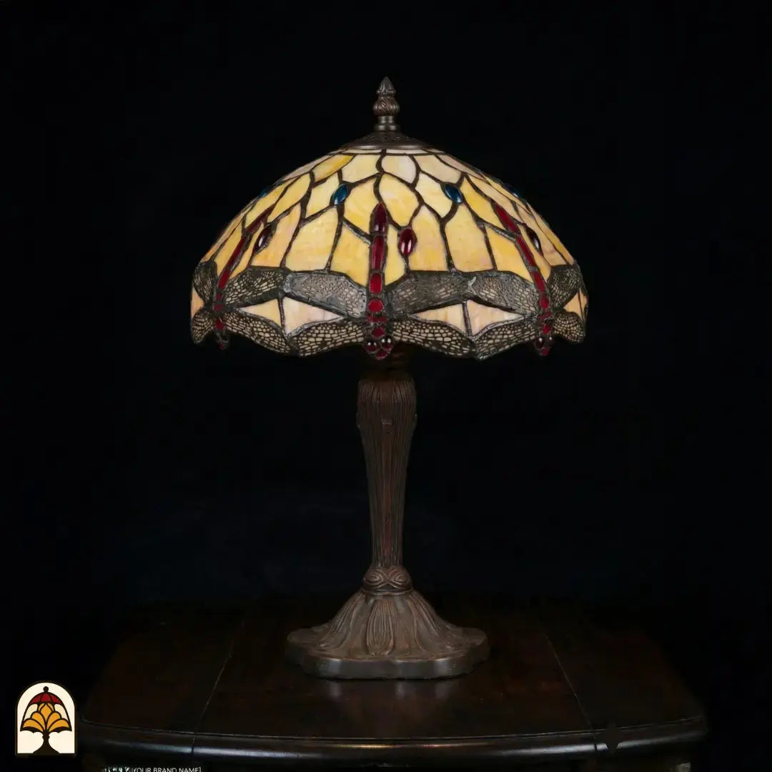 Onverlichte Tiffany tafellamp Libelle Elegance op donkere achtergrond, geel-amber kap met libellenmotieven langs de rand, bronzen geribbelde vaasvoet