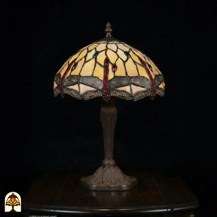 Onverlichte Tiffany tafellamp Libelle Elegance op donkere achtergrond, geel-amber kap met libellenmotieven langs de rand, bronzen geribbelde vaasvoet